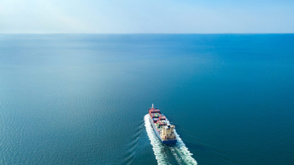 Aerial view from drone, Cargo vessel sail to the sea with peaceful wave in beautiful scenic sky. Professional business logistics and transportation of cargo ship.