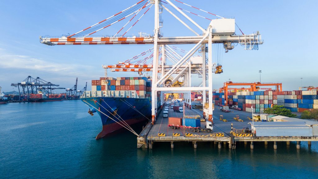 gantry cranes loading cargo container ship at a busy commercial port terminal, with trailer trucks lined up on the dock to support global maritime logistics and supply chain operations.
